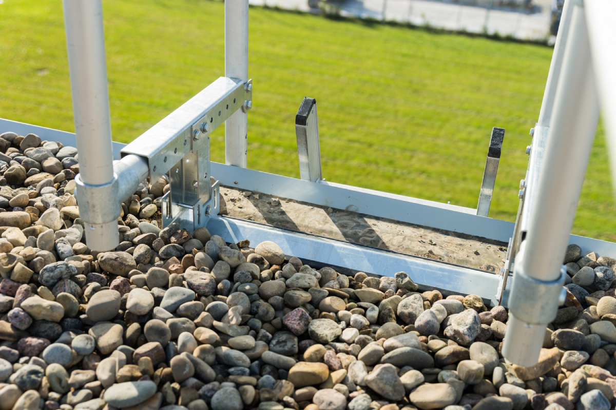 A ladder stabilizer installed on a roof with gravel.
